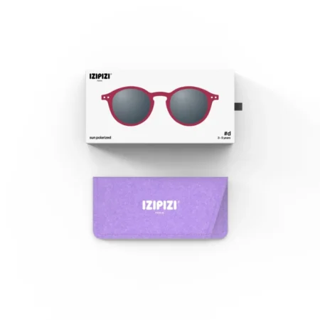 Round red sunglasses with dark lenses mounted on a white IZIPIZI box, accompanied by a purple carrying case.