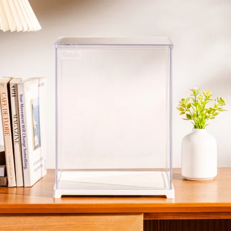 Clear acrylic display case sits on a wooden desk, with a white vase of yellow flowers to the right and books on the left.
