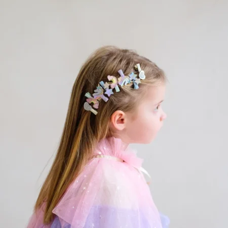 Side profile of a young girl in a pastel pink-to-lavender tulle dress, with colorful decorative clips in her hair above the ear.