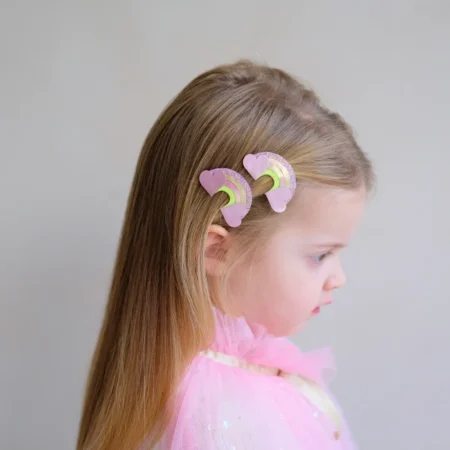 Side profile of a young girl with two pink heart-shaped hair curlers clipped in her hair through the left temple area, wearing a pink outfit.