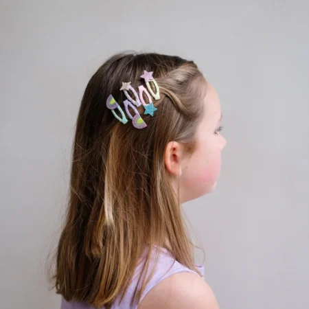 Side profile of a young girl with brown hair, wearing pastel glitter hair clips arranged in a word along the top of her head with star shapes nearby.