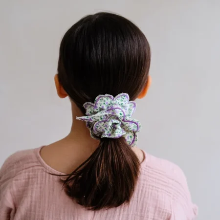 Back view of a girl with a pastel pink top and a purple-green flower hair clip securing a low ponytail.