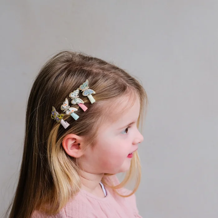 182037-23-floral-butterfly-mini-clips_699425c37cb8c_700x700r Side profile of a young girl with colorful butterfly hair clips in her hair, wearing a pale pink top.