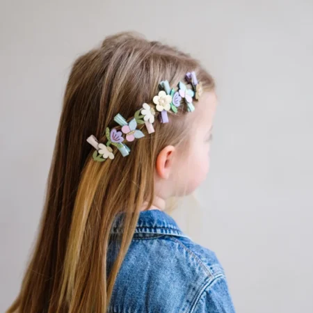 Young girl seen from behind with a pastel flower headband in her light brown hair, wearing a denim jacket.
