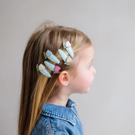 Side profile of a young girl with blue corn-shaped hair clips and pastel leaves in her hair.