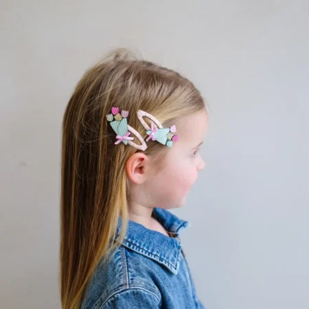 Side view of a young girl with long blonde hair wearing pastel flower/dreamcatcher hair clips and a denim jacket.
