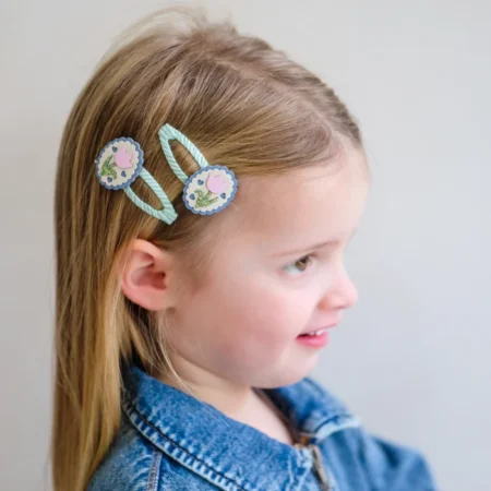 Young girl wearing blue floral hair clips with turquoise ribbons in her hair, side profile view.