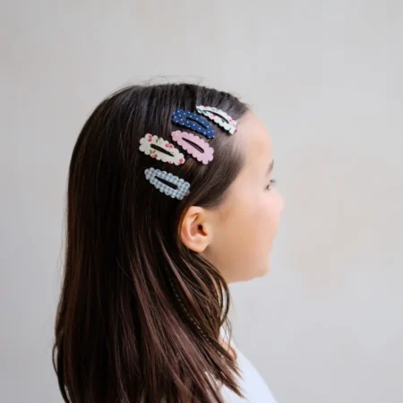 Side profile of a young girl with six decorative hair clips in blue, pink, and white patterns in her dark hair.