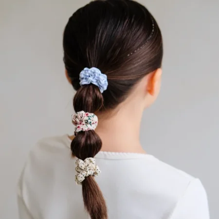 Woman with dark brown hair in a low braided ponytail, wrapped with blue scrunchie and floral-patterned scrunchies along the braid.