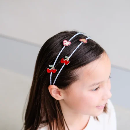 A young girl wearing two decorative headbands with red cherry and heart shapes.