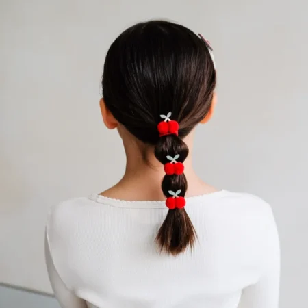 Back view of a girl with dark hair in a braided ponytail, secured with red pom-pom hair ties and small gray bows