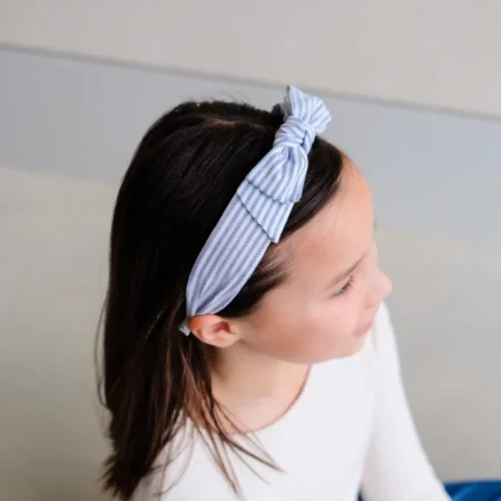 Young girl with a blue striped headband tied in a bow, viewed in profile from the left side.