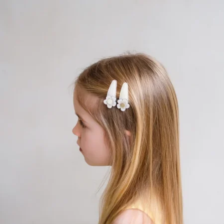 Side profile of a young girl wearing two white flower hair clips in her light brown hair