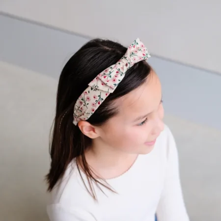 Young girl with dark hair wearing a beige floral headband tied in a knot, looking to the side.