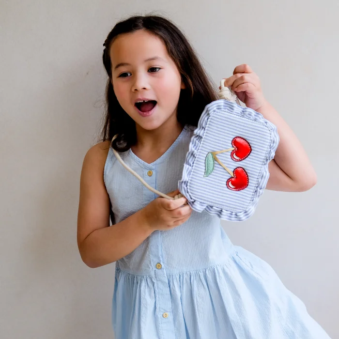 183004-10-striped-cherry-bag-2_69932a76a7a6c_700x700r Young girl in a light blue dress holds a small striped bag with red cherry decorations off to the side.