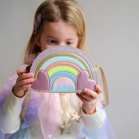 Young girl in a pastel outfit shows a rainbow-shaped mini purse with lavender clouds.