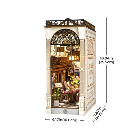 Miniature Parisian cafe diorama inside a white ornate storefront box with warm interior lighting and small tables and chairs.