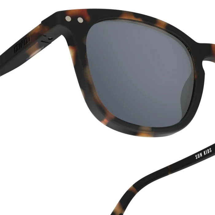 299_699db2ecae78a_700x700r Kid-sized tortoiseshell sunglasses with gray lenses, close-up on frame and temple showing 'SUN KIDS' branding.