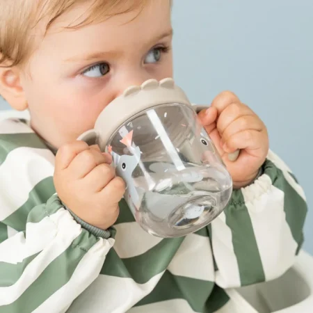 A young child sips from a clear sippy cup decorated with animal shapes, wearing a green-and-white striped jacket.