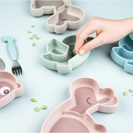 Child's hand pressing together a pastel animal-shaped cookie cutter on a light blue surface, with sprinkles nearby.