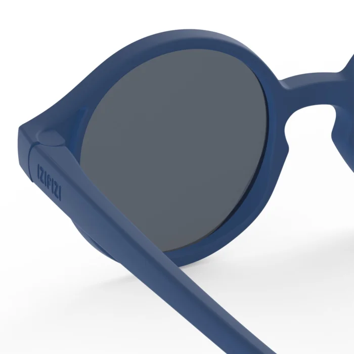 64_699c6a15ca4b4_700x700r Close-up of blue sunglasses with round dark lenses, brand name visible on the temple.
