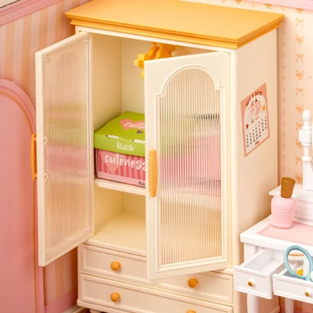 White toy wardrobe with frosted doors and orange handles, one door open to reveal folded pastel clothes on a shelf inside.