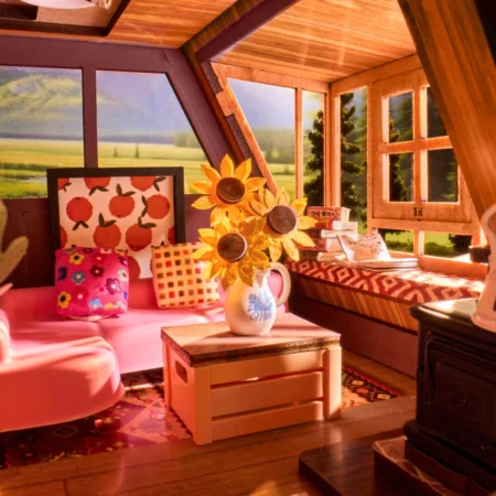 Cozy pink attic living nook with sunflowers in a vase on a white wooden coffee table and colorful pillows by a windowed wall.