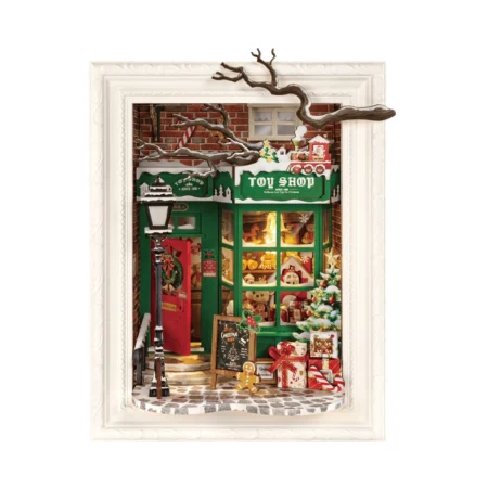 Diorama of a Christmas toy shop with a green storefront, gift-wrapped presents outside, and a chalkboard sign in frosty winter setting framed by a white border