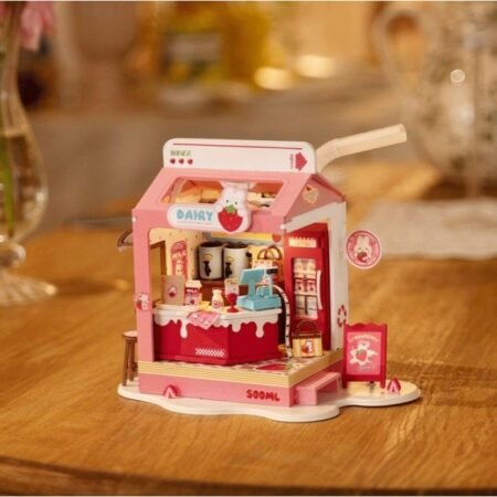 Pink toy dairy shop playset on a wooden table, with miniature drinks, milk cartons, and a cashier area.