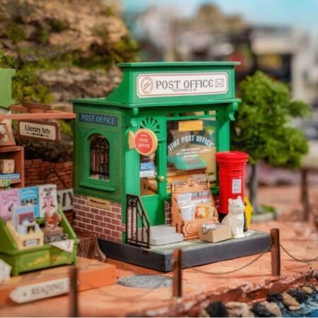 Miniature green post office storefront with a 'Post Office' sign, red mailbox, and small papers and magazines outside.