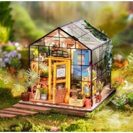 Miniature glass greenhouse on a garden lawn filled with potted plants and tiny furniture inside.