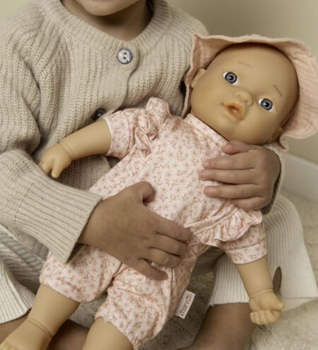 Child in a cream sweater holding a pink-clothed baby doll with blue eyes and a hat.