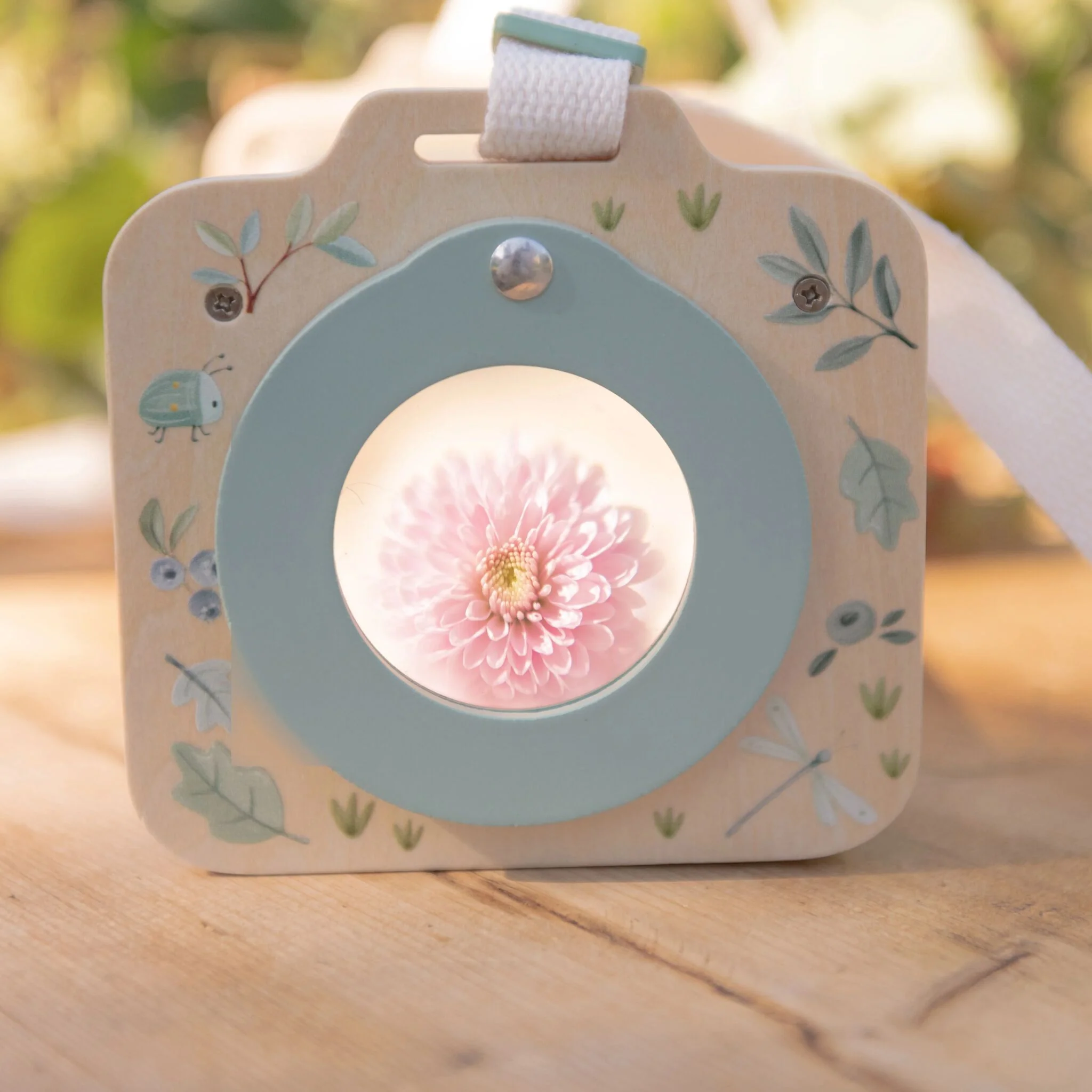 image_40804 Close-up of a wooden decorative piece with a pastel blue circle and pink flower center, surrounded by leaf patterns on a table surface.