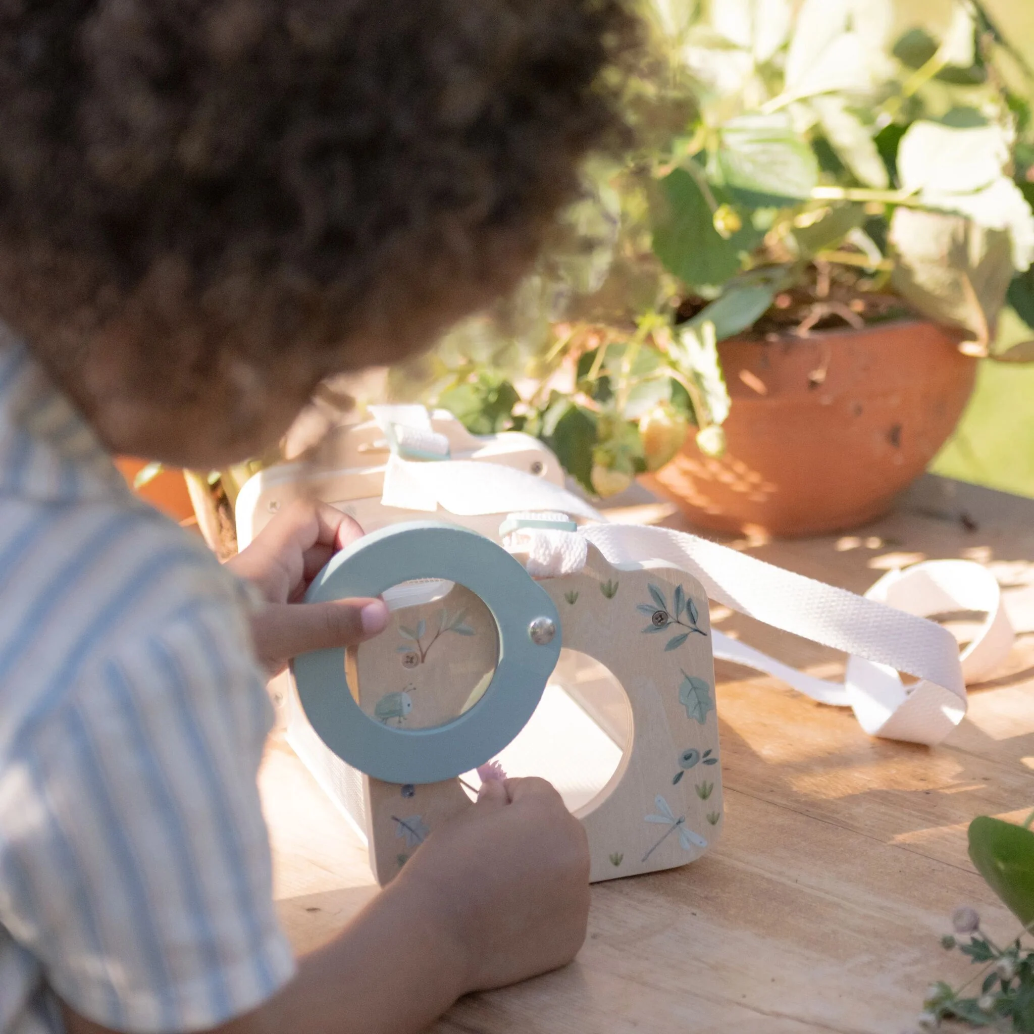 image_40805 Close-up of a baby in a blue striped shirt holding a blue circular craft on a wooden outdoor table.