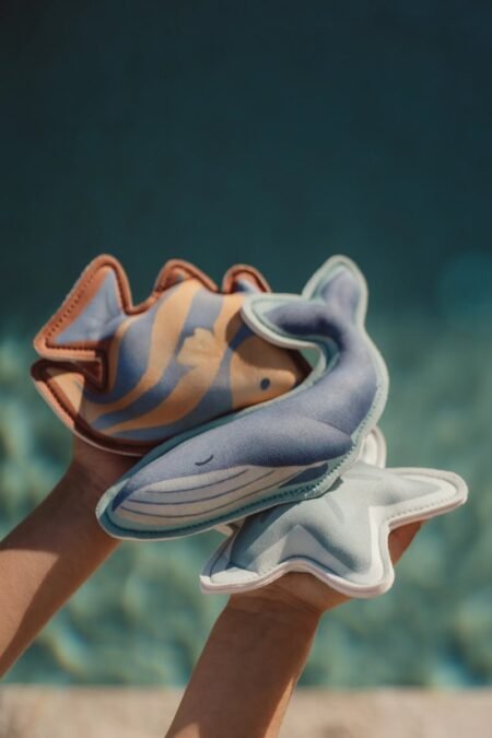 Child's hands hold three plush sea creatures—a fish, whale, and starfish—against a blurred blue ocean background.