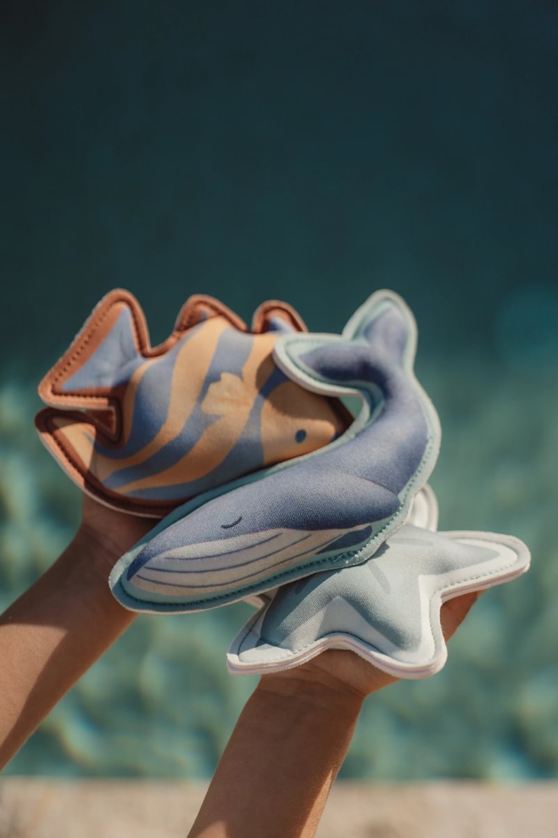 image_41647 Child's hands hold three plush sea creatures—a fish, whale, and starfish—against a blurred blue ocean background.