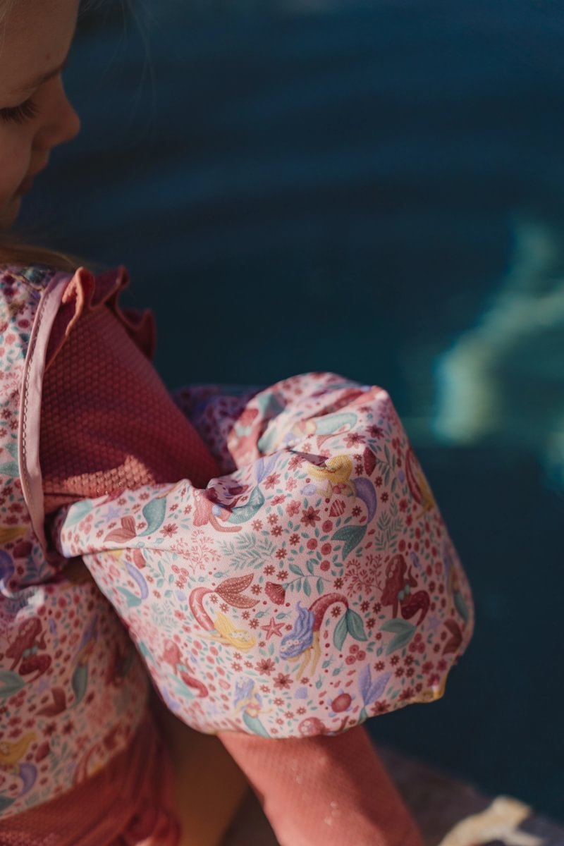 image_41673 Close-up of a child wearing a pink floral backpack on a pink sweater, against a blue background.
