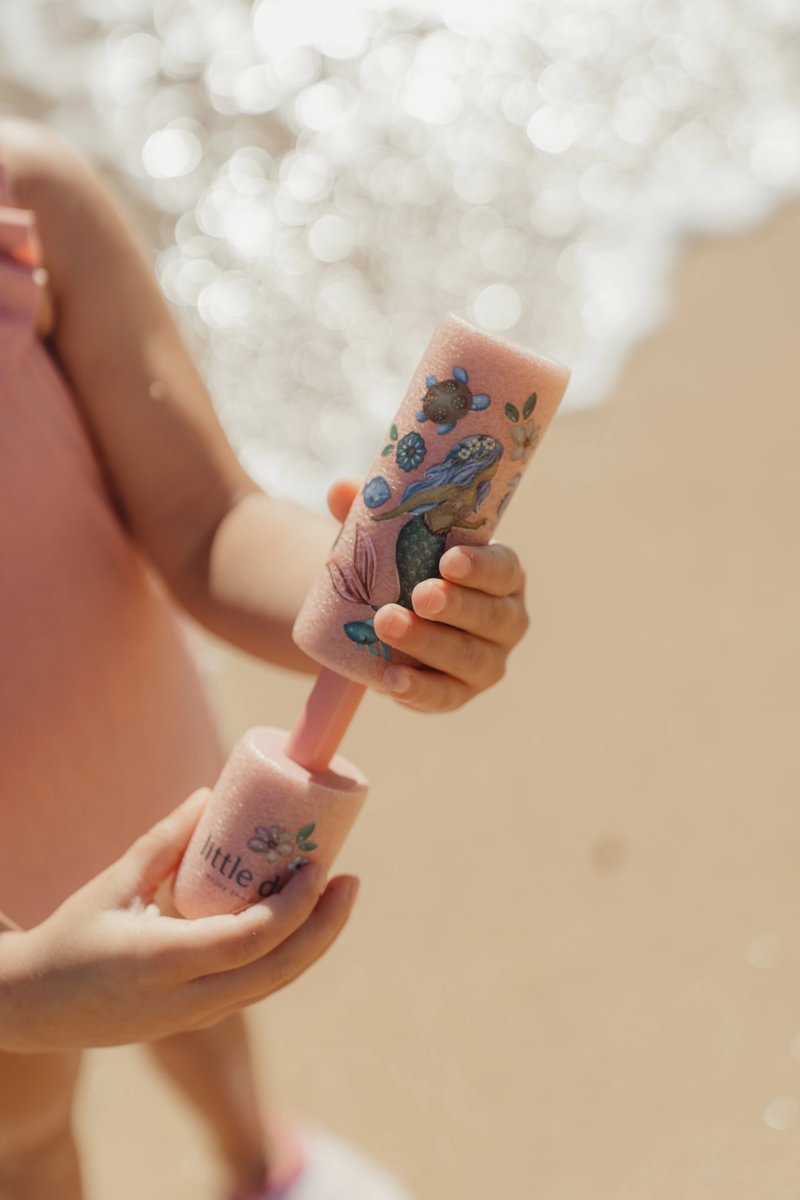 image_41767 Close-up of a child's hands holding a pink glittery roller toy with a mermaid and floral design.