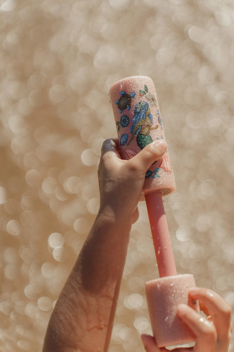 image_41768 Close-up of a child’s hand holding a pink glittery bubble wand with a sea-themed design against a sparkling background.