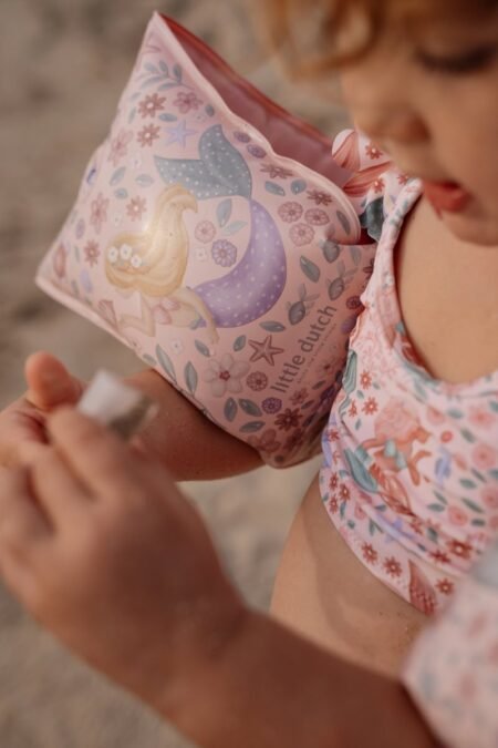 Close-up of a child wearing a pink floral swimsuit with a pastel pink inflatable arm floatie featuring a mermaid design.