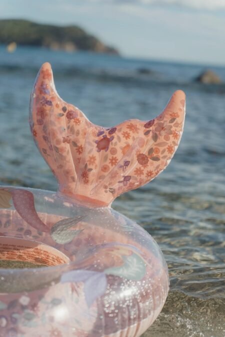 Pink floral mermaid tail inflatable float in shallow ocean water near the shore
