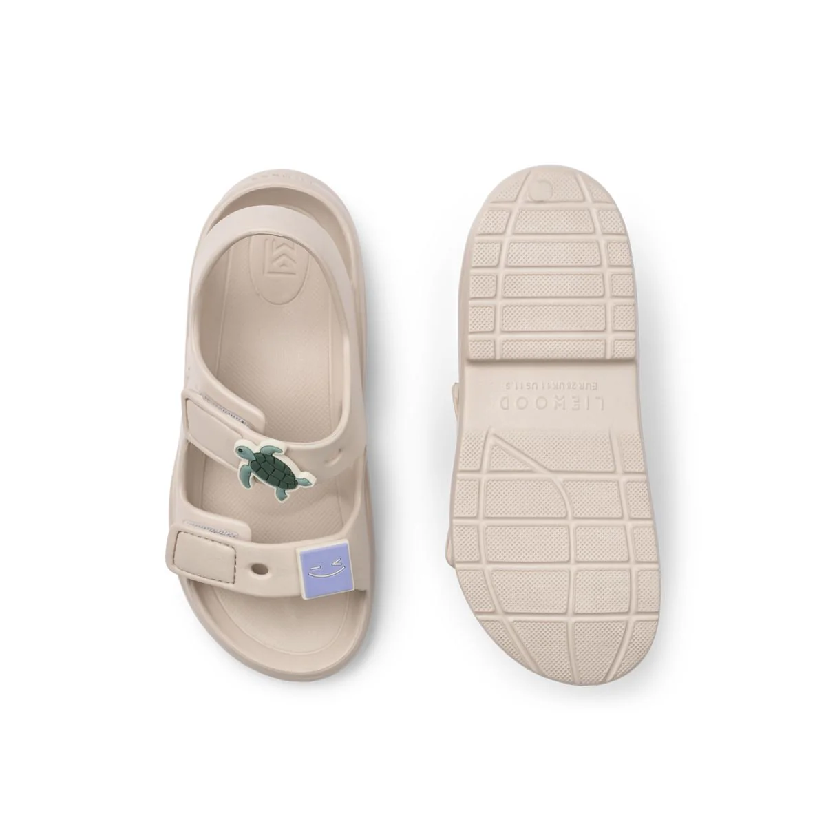 a29udGFpbmVyL25ldy80OTQ5LzE3ODU0NzU2djEucG5n Beige kids' sandals with a green turtle patch and adjustable strap, shown from the top and sole view.