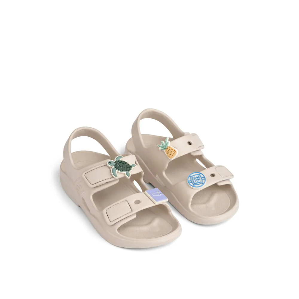 a29udGFpbmVyL25ldy80OTQ5LzE3ODU2MDQzdjEucG5n_c9427085-89b8-49ef-bf40-67aefc252abe Beige kids' sandals with two Velcro straps and decorative patches (turtle, pineapple, and blue emblem).